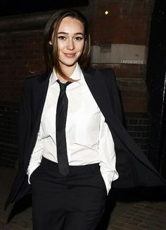 a woman in a white shirt and black tie posing for the camera with her coat over her shoulders