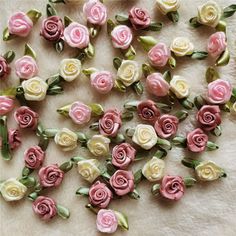 small pink and white roses are on a tablecloth with green leaves in the middle