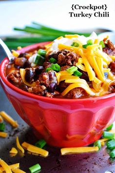 crockpot turkey chili in a red bowl with green onions and cheese on top