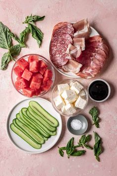 several different types of food sitting on top of a pink countertop, including cucumbers, meat and cheese