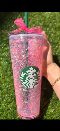 a starbucks cup with pink glitter and a bow on it's lid sitting in the grass