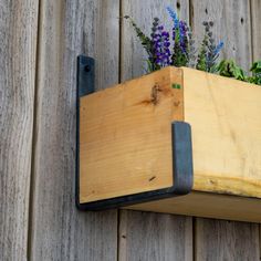 a wooden box with some plants in it on a wall mounted planter by the side of a fence