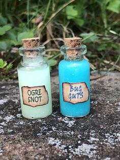 two small bottles sitting on top of a rock next to each other, one blue and the other green