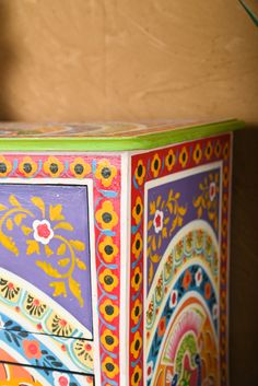 a colorful painted cabinet sitting on top of a wooden floor next to a planter