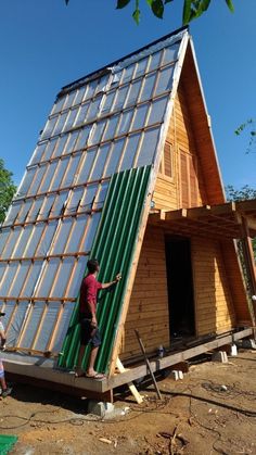 two people are standing on the roof of a small wooden house that is being built