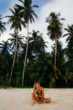 a woman sitting on the beach in front of palm trees