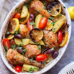 chicken with lemons, tomatoes and olives in a white casserole dish