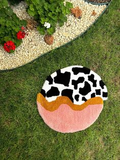 a cow print rug sitting on top of a grass covered ground next to flowers and plants