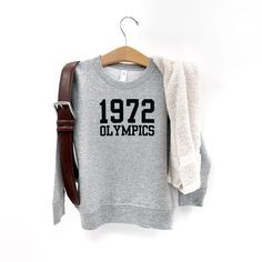 Channel your inner Miss Trunchbull with this 1972 Olympics sweatshirt. Not just for Halloween, this classic sweatshirt is perfect for any time of the year and doubles as an epic costume. Don't miss out on the funniest and most adorable wardrobe addition!! Retro Long Sleeve Pre-shrunk Sweatshirt, Retro Crew Neck Hoodie For Fall, Retro Fall Sweatshirt For Loungewear, Retro Crew Neck Sweatshirt For Loungewear, Retro Crew Sweatshirt For Fall, Retro Sweatshirt For Game Day In Winter, Vintage Fleece Tops For Fall, Retro Winter Game Day Sweatshirt, Retro Game Day Sweatshirt For Winter