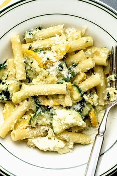 a white plate topped with pasta covered in cheese and spinach next to a fork