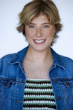 a woman with short hair wearing a jean jacket and striped shirt smiling at the camera