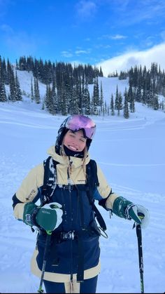 a woman standing on top of a snow covered ski slope holding skis and poles