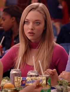 a woman sitting at a table with drinks and food in front of her, looking surprised