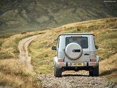 a jeep driving down a dirt road in the middle of a grassy hill side area