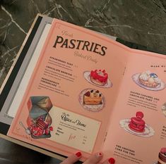 an open book with pictures of pastries and desserts on the pages in front of a woman's hand