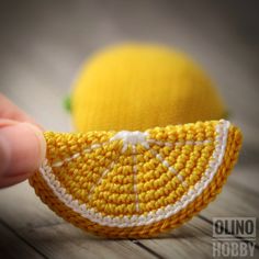 a hand is holding a small crocheted yellow object with white stitching on it