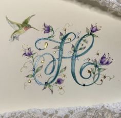 the letter h is decorated with purple flowers and a humming on it's side