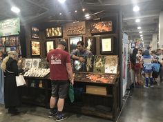 people looking at items on display in an indoor exhibit area with lights overhead and lots of posters hanging from the ceiling