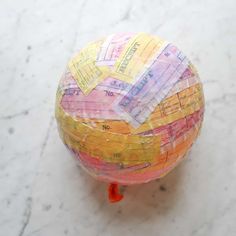 a paper mache ball sitting on top of a marble floor covered in colorful papers