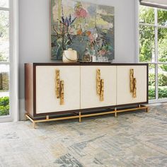 a white and brown cabinet with gold handles in front of a painting on the wall