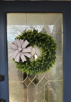 a green wreath with a bow hanging on a blue front door glass paneled in