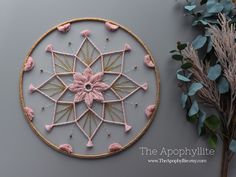 a pink and gold wall hanging next to some flowers