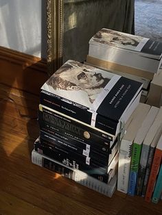 a stack of books sitting on top of a wooden floor next to a window with curtains