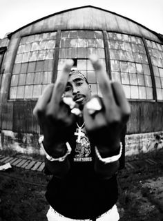 a black and white photo of a man making the v sign with his hands in front of a building