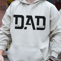 a man wearing a white hoodie with the word dad printed on it and his hands in his pockets