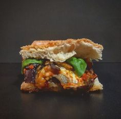 a sandwich with meat, cheese and vegetables is on a black surface in front of a dark background