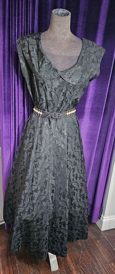 "Note:  this dress was clipped to fit my mannequin. It is displayed with a soft crinoline underneath. This pretty black on black satin dress with its Audrey Hepburn-esque portrait collar is in excellent vintage condition. There is a soft shoulder pad on each side. Please be sure to note the beautiful black on black fabric with its floral motif; note, too, the black satin belt with its 5\" long faux opal and goldmetal detail on each end of the belt. Approximate measurements: shoulder to shoulder: Gothic Sleeveless Formal Dress, Gothic A-line Formal Dress, Fitted Gothic Evening Dress For Formal Events, Elegant Black Vintage Dress For Party, Elegant Black Vintage Party Dress, Elegant Black Vintage Dress, Black A-line Vintage Dress For Evening, Elegant Black Vintage Dress For Formal Occasions, Elegant Black Vintage Evening Dress