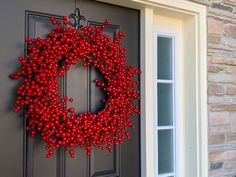 a red berry wreath on the front door of a house with grey doors and windows