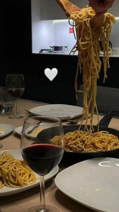 a table topped with plates of spaghetti and glasses of red wine next to each other