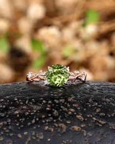 an engagement ring with a green stone surrounded by leaves and flowers on top of a rock