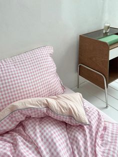 a pink and white checkered comforter on a bed next to a night stand