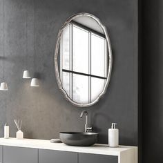 a bathroom with a round mirror above the sink and gray walls, along with white fixtures