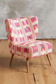 a pink and white chair sitting on top of a wooden floor next to a wall