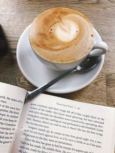 a cup of coffee on top of a white saucer next to an open book