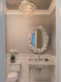 a white toilet sitting next to a bathroom sink under a round mirror on the wall