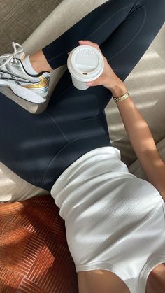 a woman laying on top of a bed holding a coffee cup in her right hand