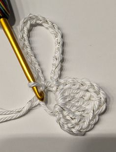 a crochet hook with a gold colored handle and white yarn around it on a table