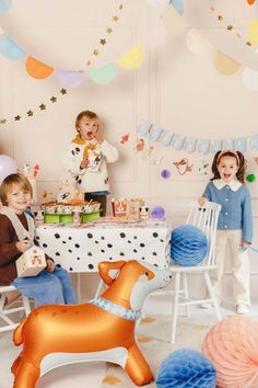 three children are sitting at a table with balloons and decorations in the shape of animals