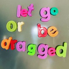 the words let go or be dragged written in multicolored plastic letters on a stainless steel surface