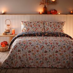 a bed covered in a floral comforter next to candles and pumpkins on the floor