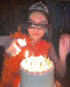 a woman wearing glasses and a tiara is blowing out candles on her birthday cake