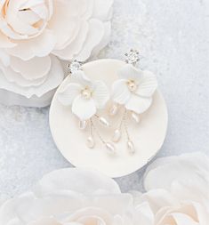 two white flowers and pearls are sitting on a plate next to the flower petals in front of them