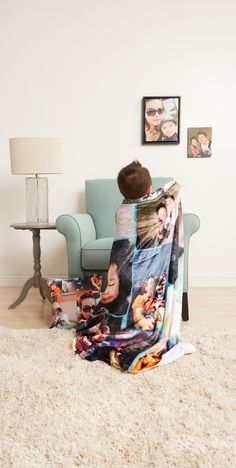 a young boy is sitting on a couch wrapped in a blanket and looking at pictures