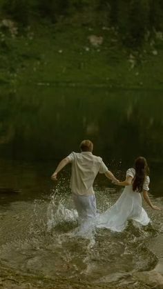 a man and woman are walking through the water in their wedding dress, with one holding the other's hand