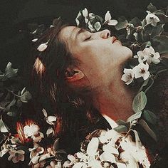 a woman with flowers in her hair is looking up at the sky while she's surrounded by leaves and flowers