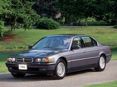 a black car parked on the side of a road in front of some grass and trees